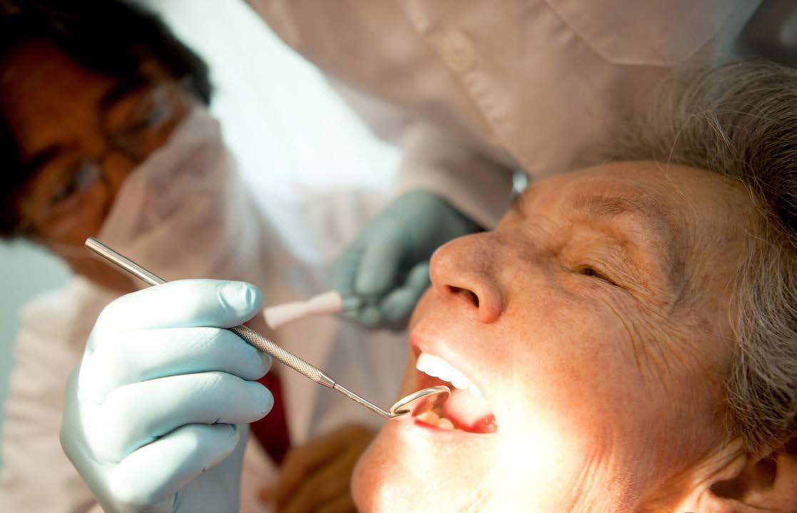 The image shows a person receiving dental care, with a dentist performing a procedure on the patient s mouth using dental instruments.