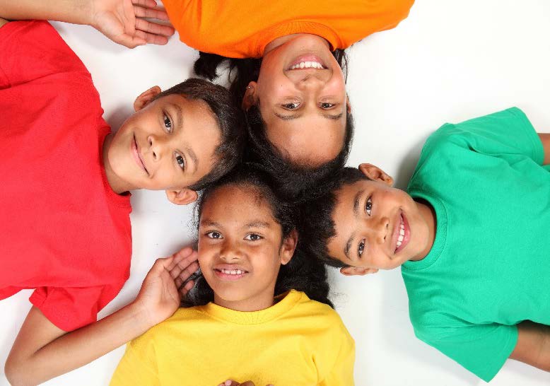 The image shows a group of four children with different colored shirts sitting on the floor, smiling at the camera.