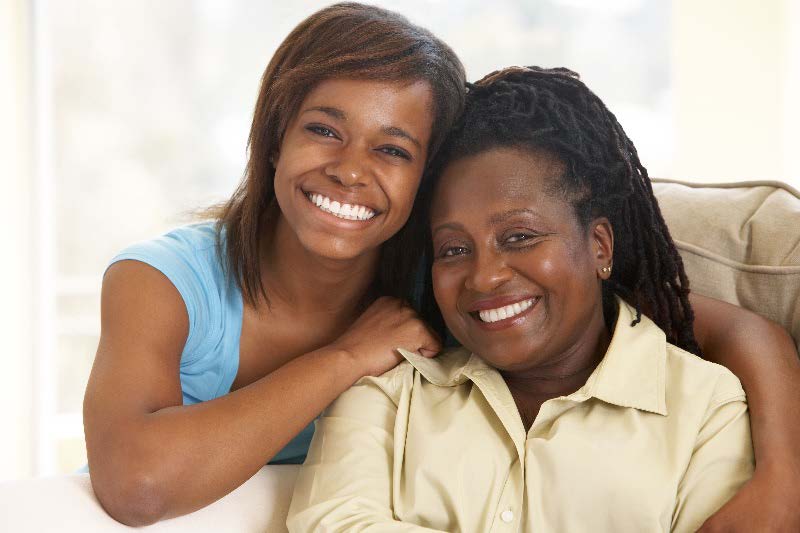 A young woman and an older woman share a warm embrace on a couch.