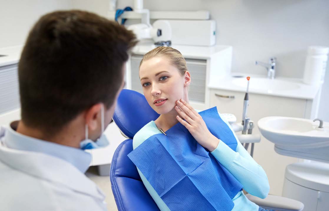 A dental hygienist in a blue gown and a patient in a dental chair, with the hygienist performing a cleaning procedure.