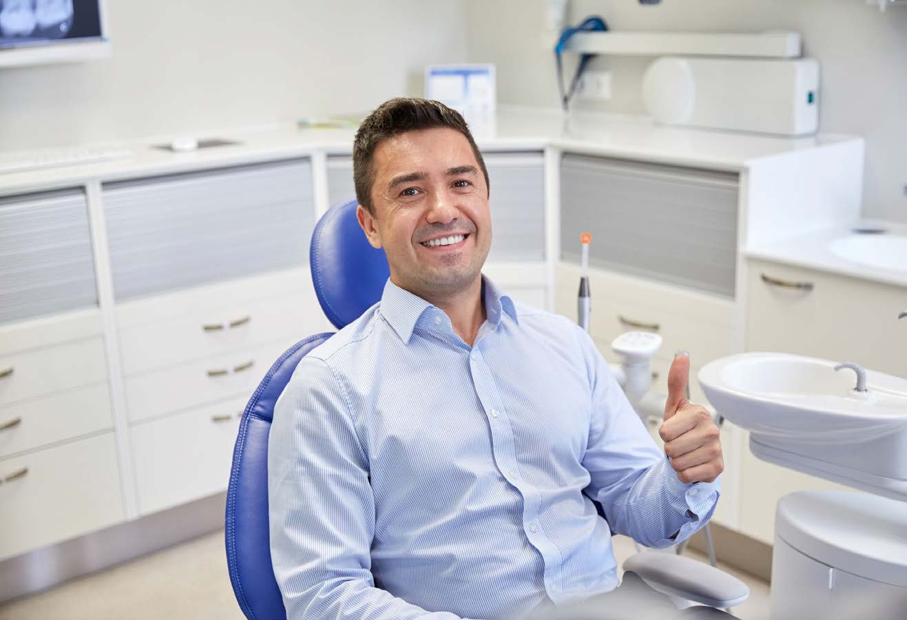 Man sitting in dental chair, smiling and thumbs up.