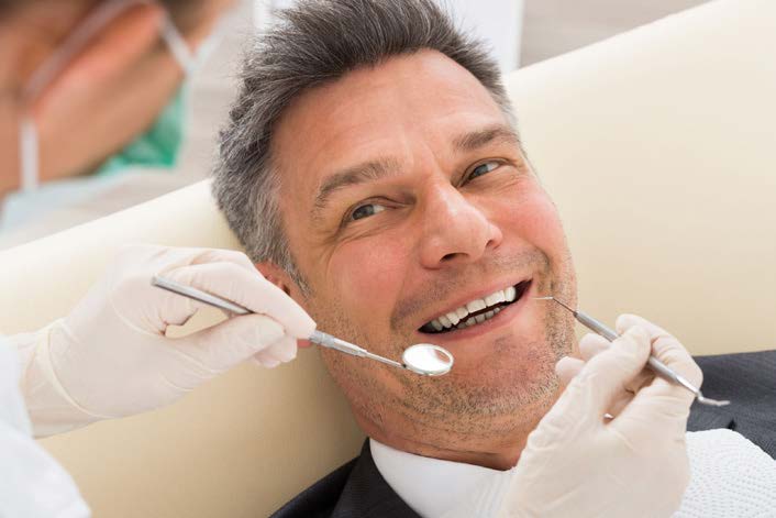 A man in a dental chair, smiling, as a dentist works on his teeth.