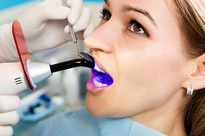 The image shows a person receiving dental treatment, with a dental professional using a device to examine their teeth.