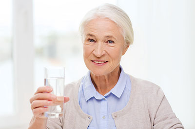 The image shows a woman holding a clear glass of water, smiling at the camera.