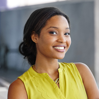 The image features a young woman with dark hair, wearing a yellow top and smiling. She is standing against a neutral background.