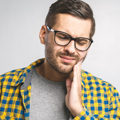 A man with a beard, wearing glasses and a plaid shirt, holds his hand to his mouth in a gesture of disbelief or pain.