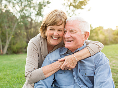An elderly couple embracing each other outdoors during the day.