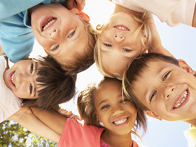 The image displays a group of children, possibly siblings, posing for a photo with their arms around each other s shoulders. They are outdoors on what appears to be a sunny day, and all the children are smiling.