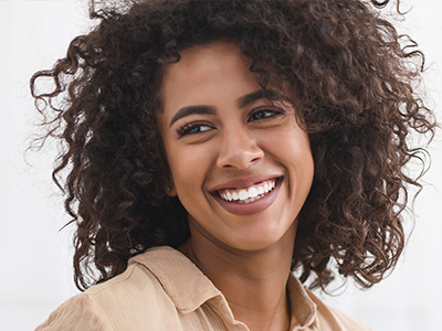 The image shows a smiling woman with curly hair, wearing a light-colored top.
